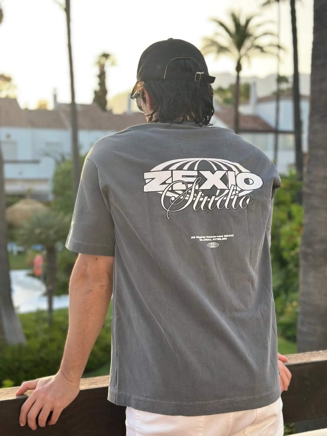 Hombre de espaldas llevando puesta una camiseta de Zexio Studio gris mirando el jardín de una casa de lujo
